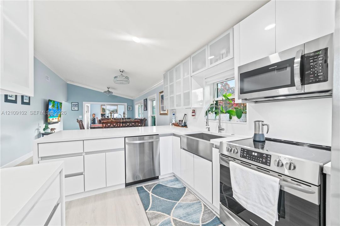 Kitchen featuring white cabinetry with glass-panel upper doors, stainless steel farmhouse sink, quartz-style countertops, and stainless steel appliances