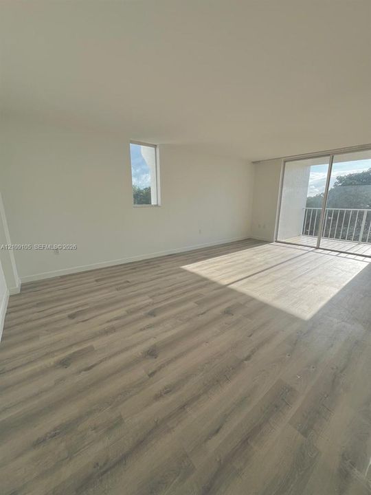 Interior space featuring wood-finish flooring, sliding glass patio doors, a private balcony with metal railing, and high-impact windows