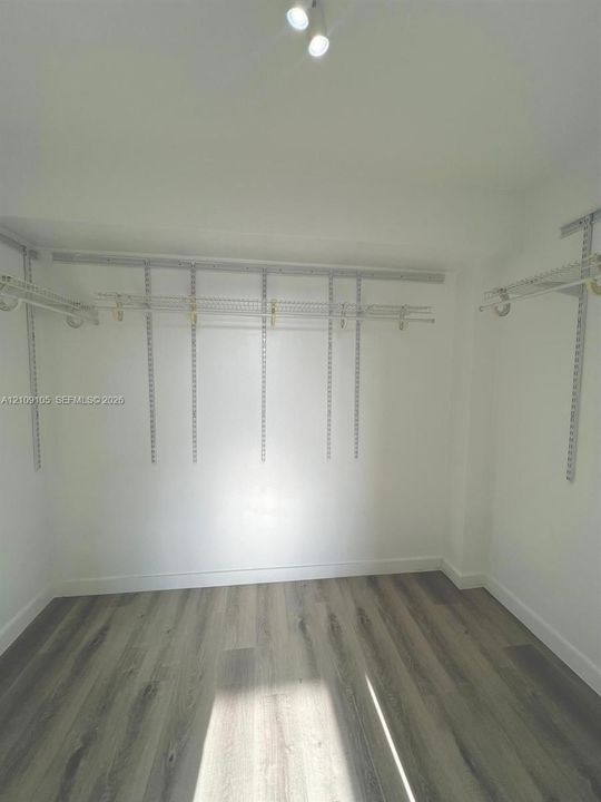 Storage area featuring wood-finish flooring, adjustable metal shelving systems, and overhead dual-bulb lighting