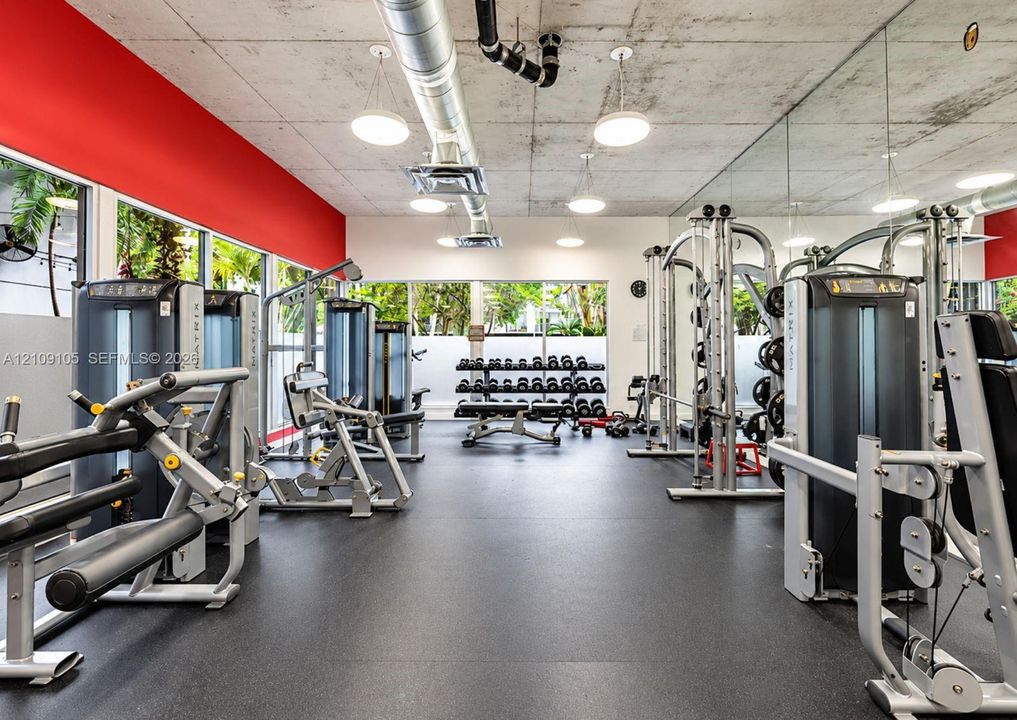 Fitness center featuring an exposed concrete ceiling, industrial ductwork, wall-to-wall mirrors, rubber flooring, and expansive windows