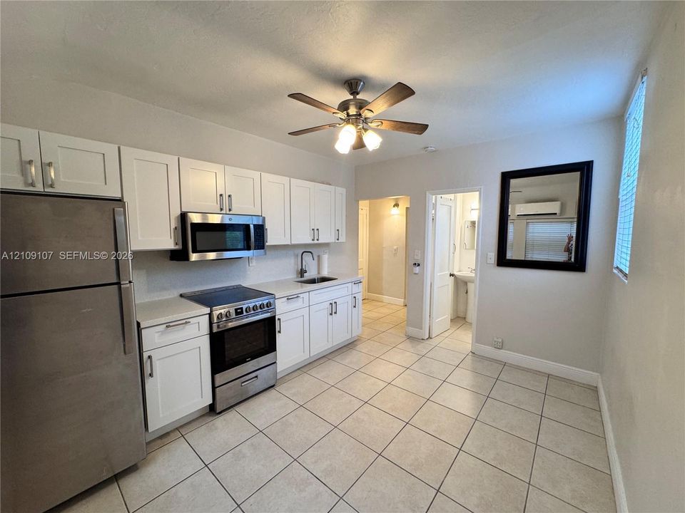 Kitchen featuring white shaker-style cabinetry, stainless steel appliances, neutral tile flooring, and a ceiling-mounted fan with integrated lighting