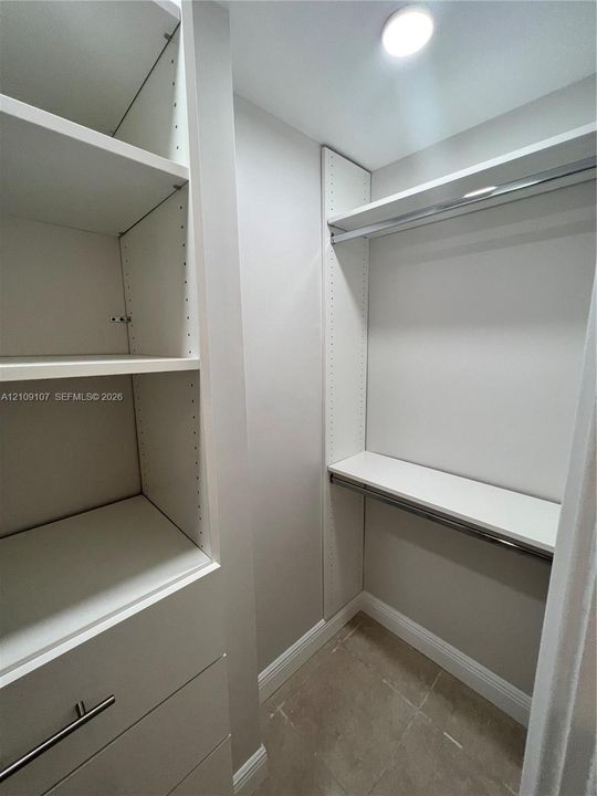 Customized built-in cabinetry featuring white shelving, integrated hanging rods, and drawers with metallic hardware