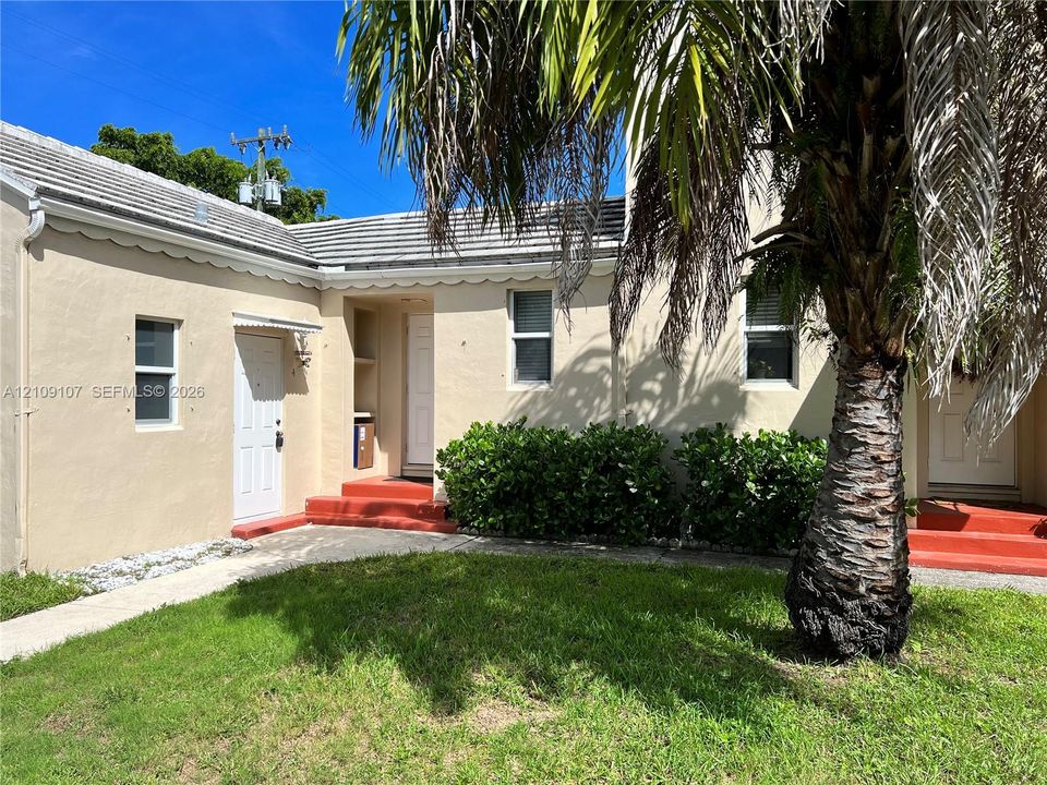 Exterior facade featuring a stucco finish, shingled roofing with scalloped eaves, concrete entry steps, and mature palm tree
