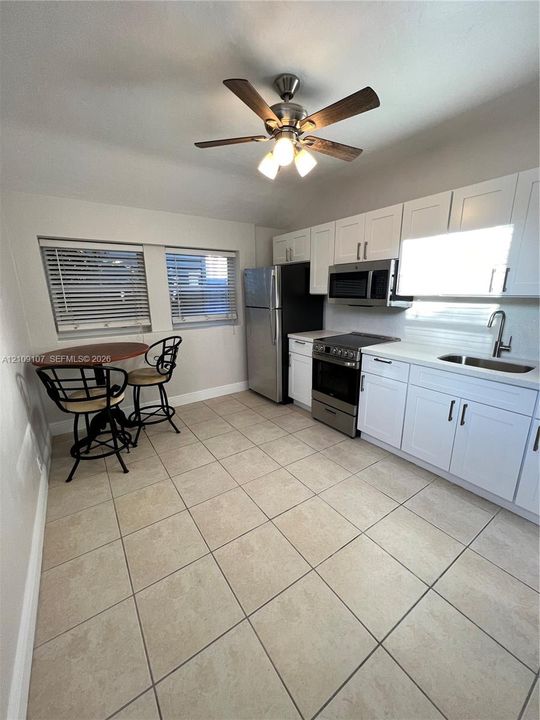 Kitchen featuring white cabinetry, stainless steel appliances, ceramic tile flooring, and a ceiling fan with integrated lighting