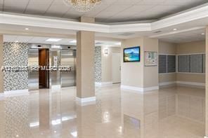 Lobby featuring polished tile flooring, metallic elevators with decorative tile surrounds, recessed lighting, and a tiered crystal chandelier