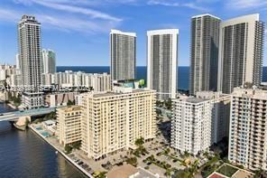 Aerial perspective of a high-density urban corridor featuring multiple high-rise towers, proximity to a waterway, and coastal horizon