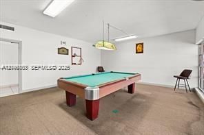 Interior space featuring neutral-toned carpeting, rectangular recessed overhead lighting, and a hanging geometric light fixture