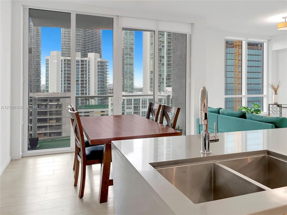 Kitchen island featuring a dual-basin stainless steel sink with a high-arch faucet, complemented by light-toned, solid-surface countertops, wood-finish flooring, and floor-to-ceiling glass sliding doors