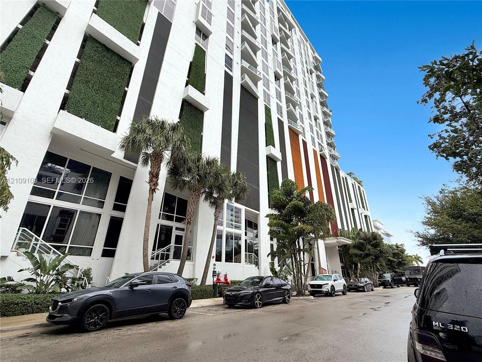 High-rise exterior featuring a multi-story facade with vertical green walls, contrasting color accents, expansive floor-to-ceiling windows, and integrated balconies