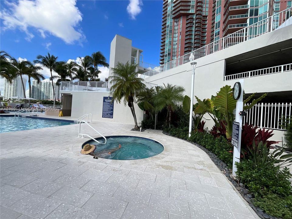 In-ground hot tub featuring stone tile surround, swimming pool, and tropical landscaping