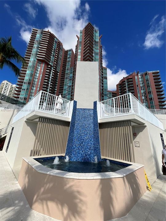 Cascading water feature with blue mosaic tiling, multi-story high-rise architecture, white metal railings, and concrete hardscaping