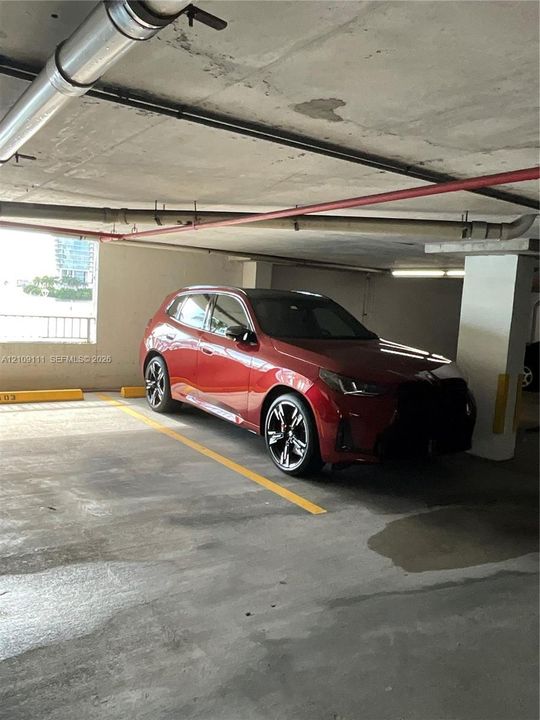 Covered parking structure featuring concrete flooring, structural support columns, and overhead utility piping
