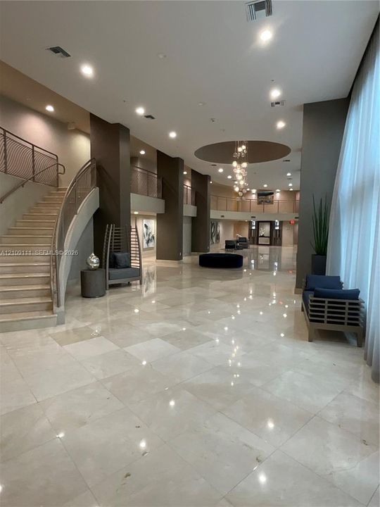 Grand entrance hall featuring high ceilings, stone tile flooring, a multi-tiered glass chandelier, a sweeping staircase with custom metal railings, and a tiered mezzanine level