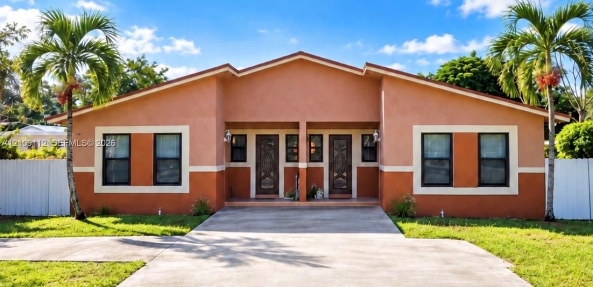 Single-story exterior featuring a dual-toned stucco facade, decorative entry doors, concrete driveway, and white privacy fencing