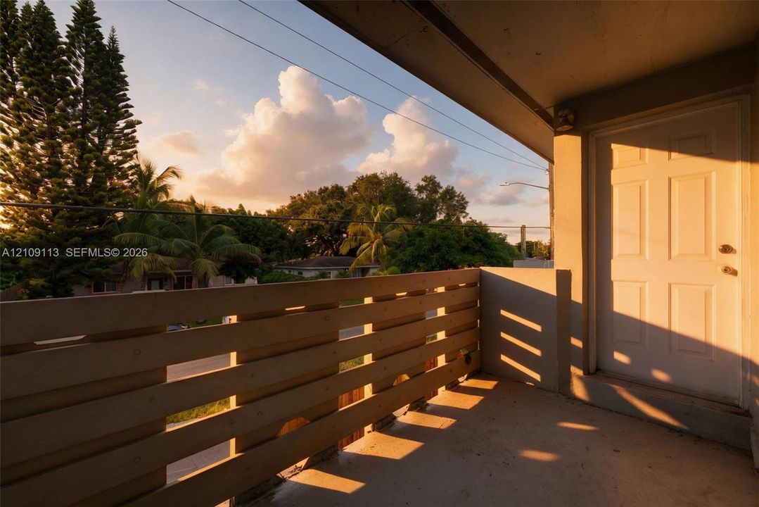 Covered balcony featuring horizontal wood-slat railings, concrete flooring, and a six-panel exterior door