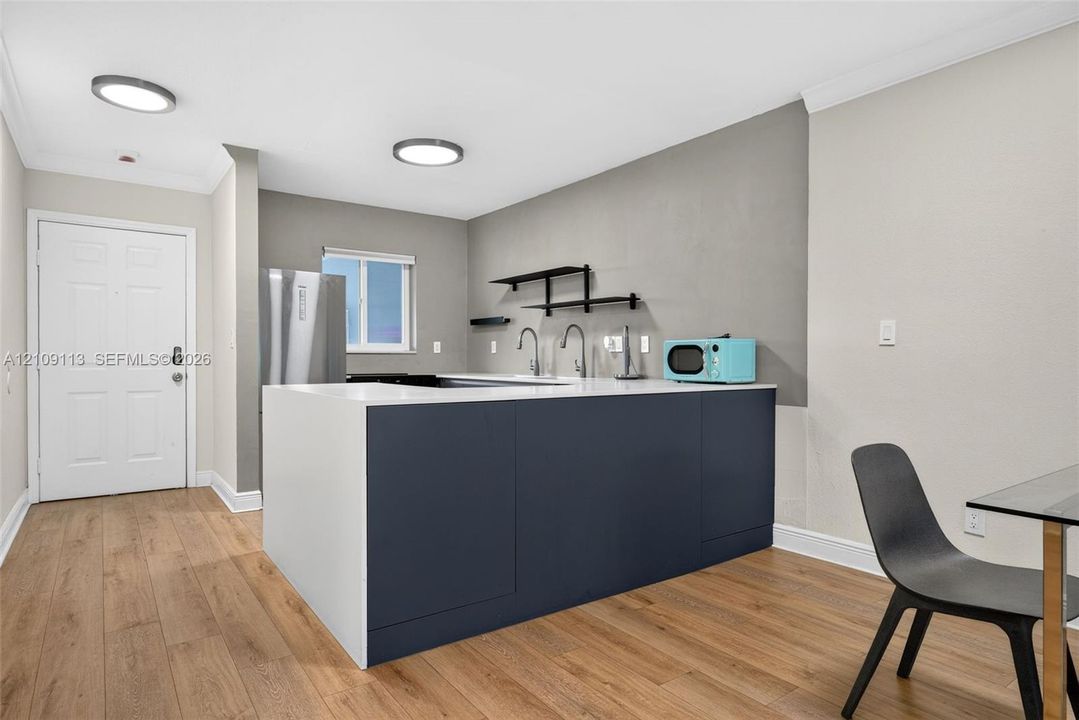 Kitchen featuring a matte dark blue island, white solid-surface countertop, wood-finish flooring, stainless steel appliances, and wall-mounted shelving