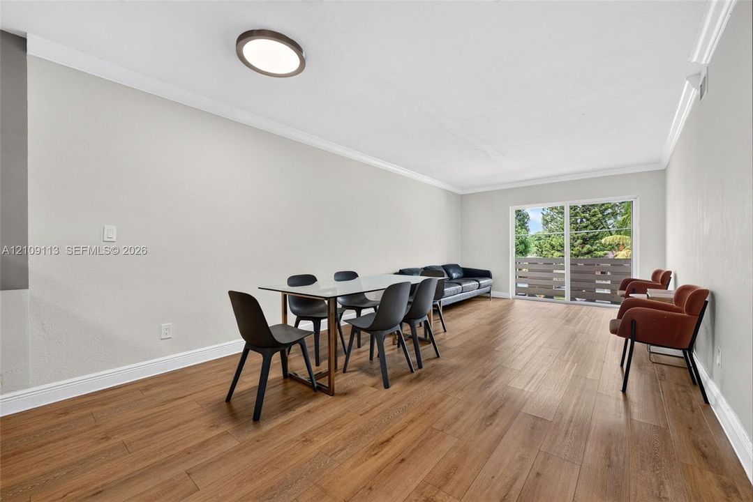 Open-concept area featuring wood-finish flooring, crown molding, a flush-mount light fixture, and sliding glass doors with a horizontal-slat balcony railing