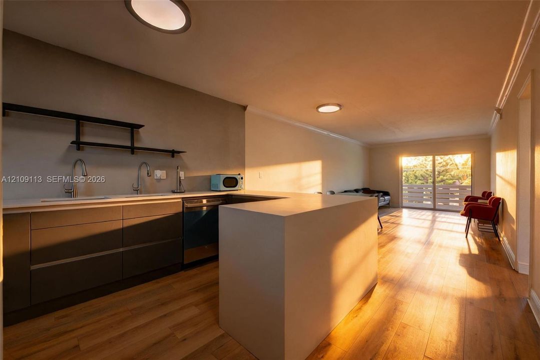 Kitchen featuring custom flat-panel cabinetry, a solid-surface peninsula, stainless steel dishwasher, wood-finish flooring, and minimalist wall-mounted shelving