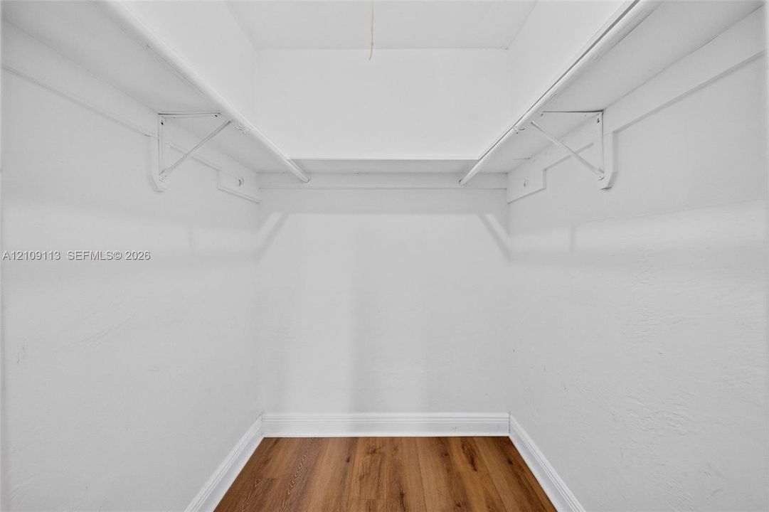 Walk-in storage space featuring wood-finish flooring and dual upper shelves with integrated hanging rods