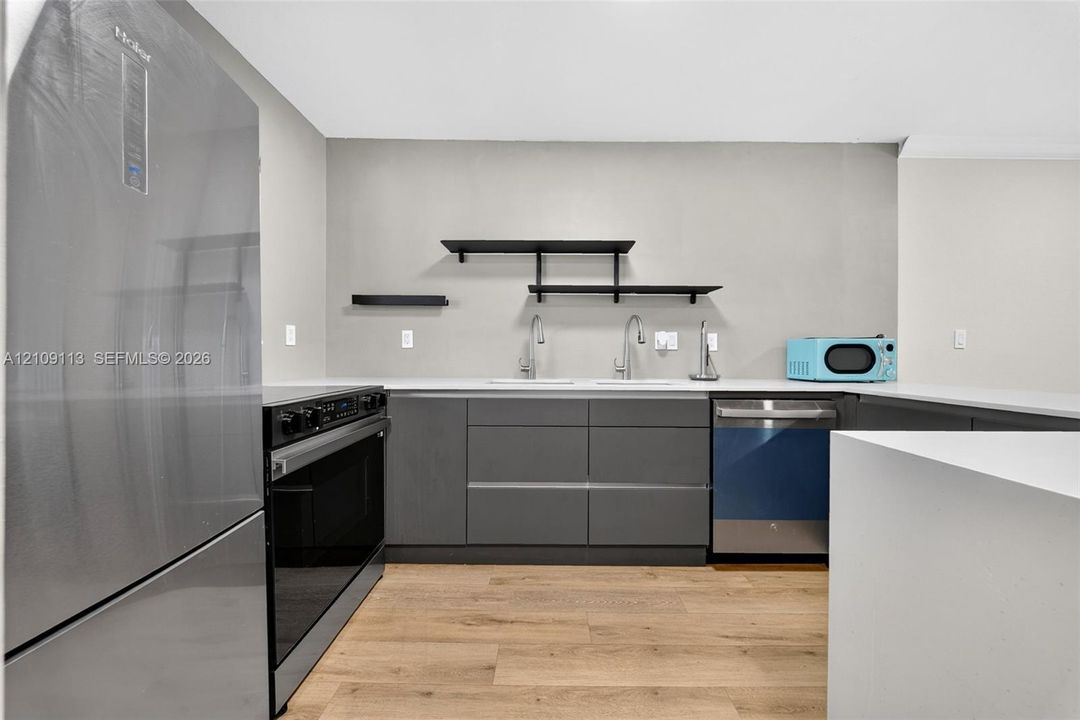 Kitchen featuring dark grey flat-panel cabinetry, white countertops, wood-finish flooring, matte black floating wall shelves, and stainless steel appliances