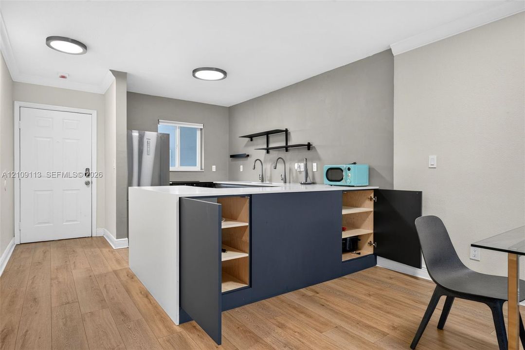 Kitchen featuring a central island with a solid surface countertop, matte finish cabinetry, wood-finish flooring, two-tone wall aesthetic, and mounted open shelving