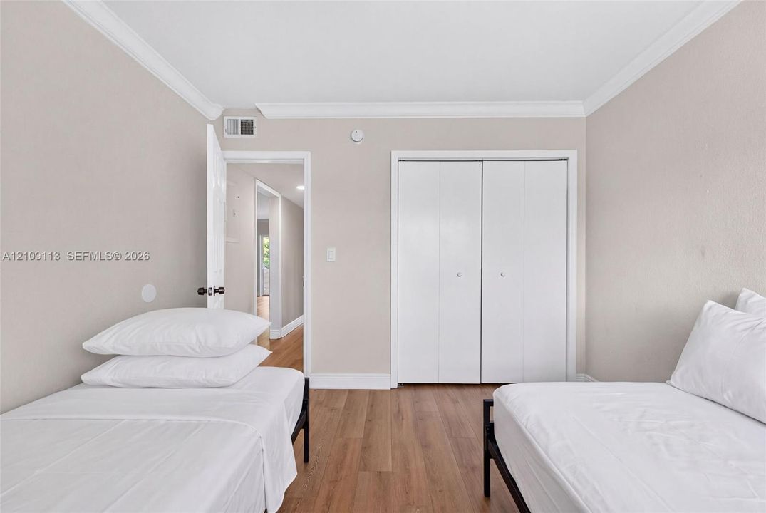 Neutral-toned interior featuring wood-finish flooring, crown molding, and double-door closet cabinetry