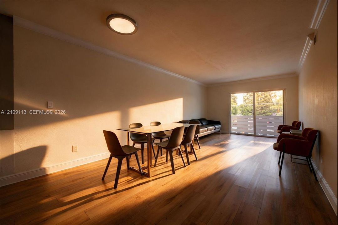 Living area featuring wood-finish flooring, crown molding, a flush-mount light fixture, and sliding glass doors with exterior railing
