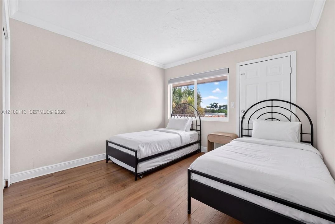 Wood-finish flooring, neutral wall tones, crown molding, and a multi-pane window with a roller shade