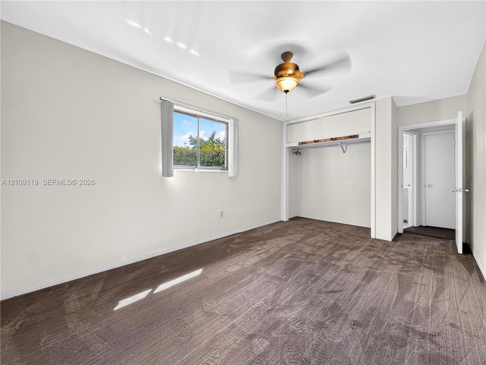Neutral carpeting, recessed closet space with integrated shelving, sliding-sash window, and central ceiling fan with integrated light fixture