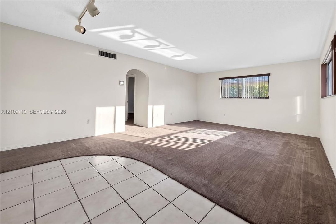 Open-concept room featuring a combination of neutral tile and wall-to-wall carpeting, an arched entryway, and adjustable ceiling-mounted track lighting
