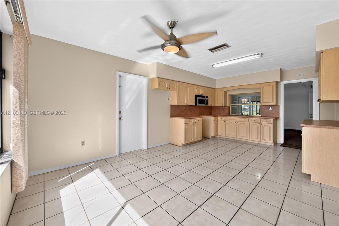 Kitchen featuring light wood-finish cabinetry, tile flooring, a built-in microwave, and an integrated ceiling fan with light fixture