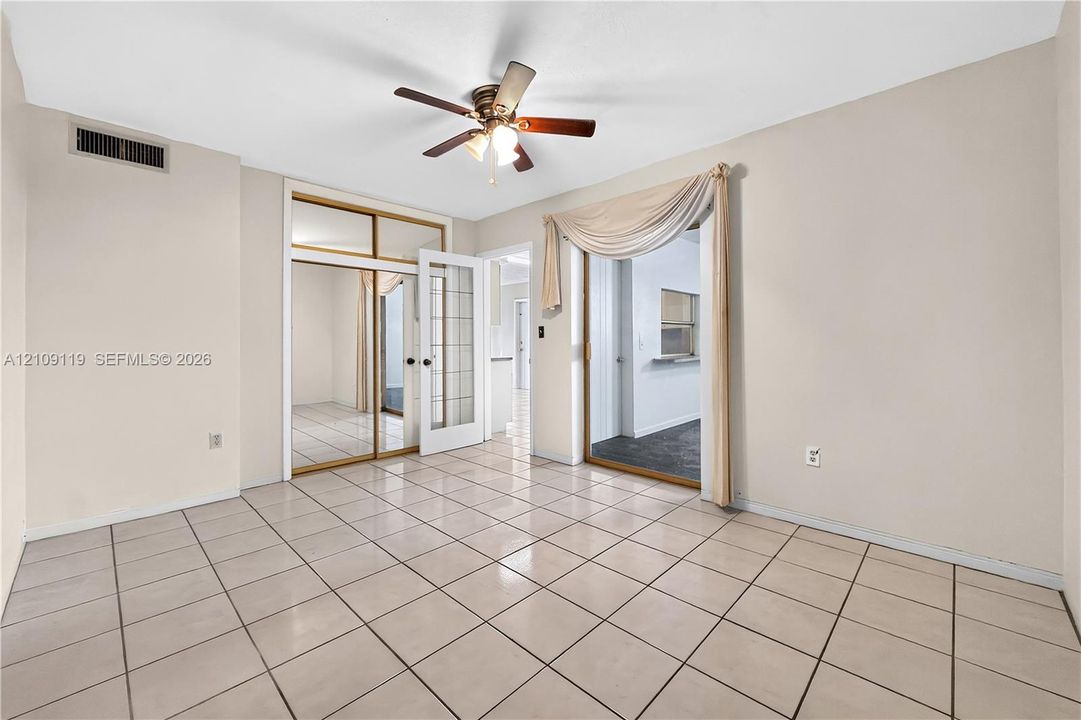 Interior space featuring light-toned tile flooring, a central ceiling fan with integrated lighting, a glass-paned French door, and a built-in closet with mirrored sliding doors