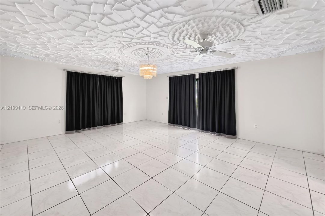 Expansive room featuring a textured decorative ceiling, dual ceiling fans, polished tile flooring, and a central tiered crystal chandelier