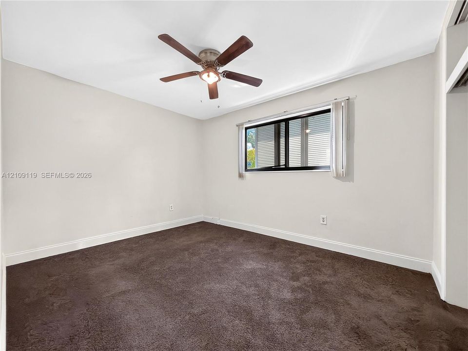 Interior space featuring neutral wall paint, wall-to-wall carpeting, a ceiling fan with integrated light fixture, and a sliding window