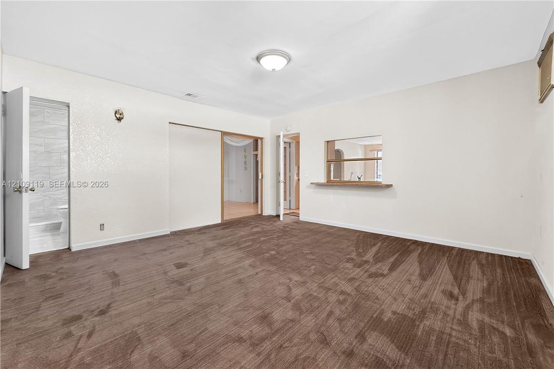 Interior room featuring wall-to-wall carpeting, flush-mount ceiling lighting, a pass-through window with a wood ledge, and a doorway revealing a tile-surround shower area