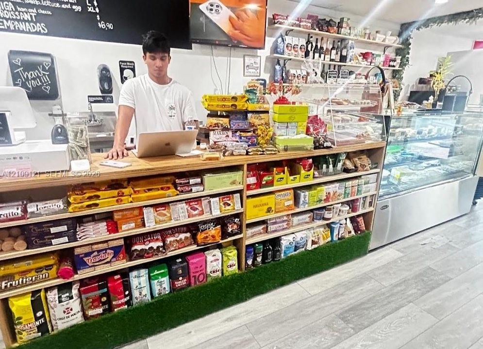 Commercial retail counter featuring light-toned wood construction, built-in shelving, artificial turf trim, and a professional-grade glass refrigerated display case