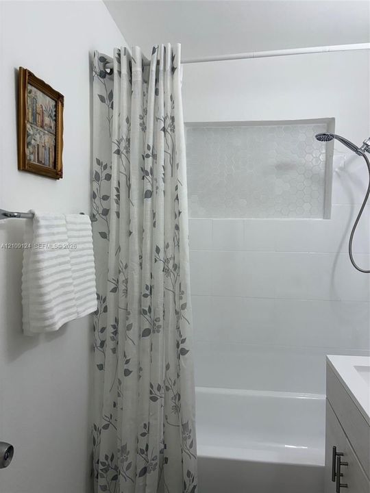 Tub and shower combination featuring a recessed wall niche with hexagonal tiling, large-format white wall tile, and a handheld shower fixture