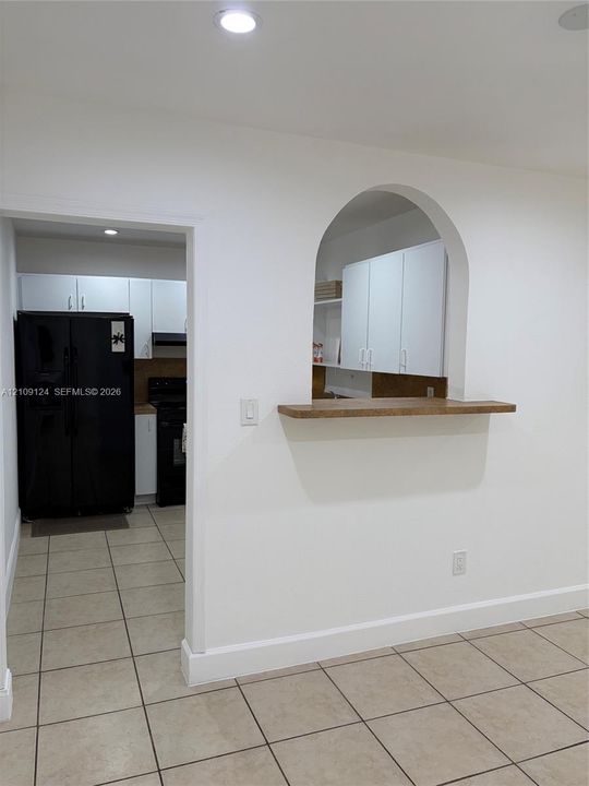 Arched pass-through featuring a wood-finish ledge, tile flooring, white cabinetry, and recessed lighting