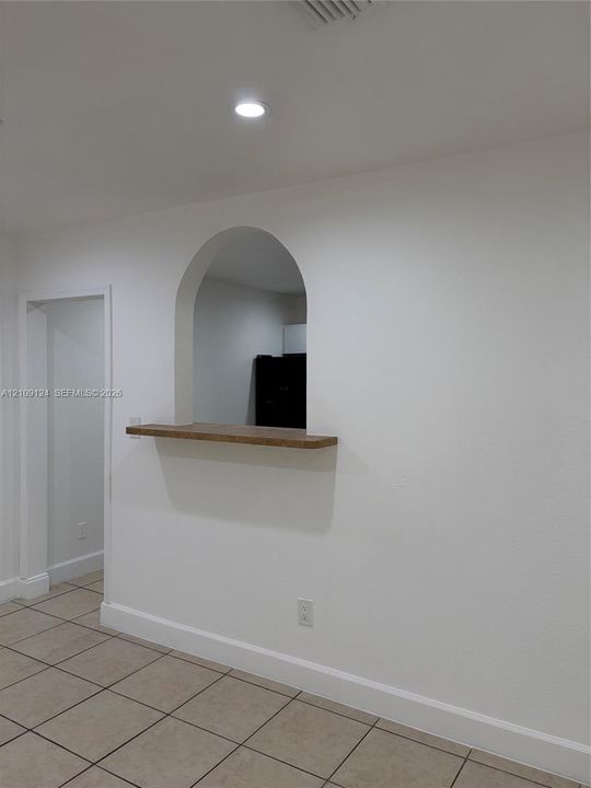Arched wall cutout featuring a wooden pass-through ledge and tile flooring