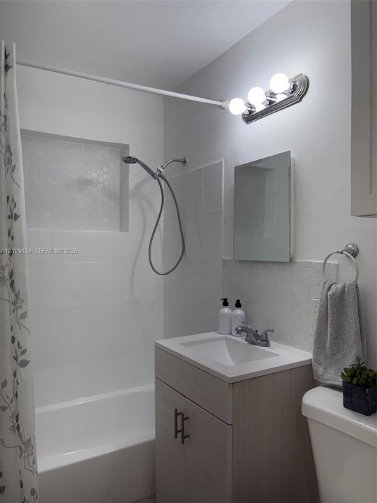 Bathroom featuring a single-sink vanity with neutral-toned cabinetry, white rectangular tiling, a built-in recessed shower niche, and a three-light vanity fixture