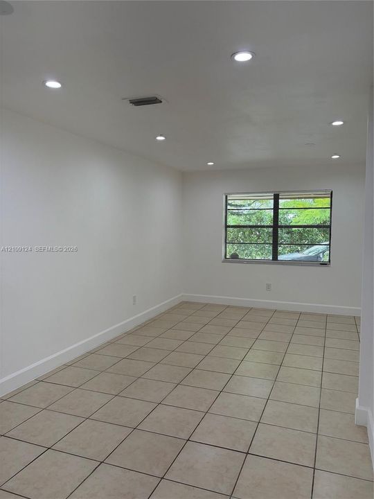 Interior space featuring neutral tile flooring, recessed lighting, and a window with black-framed panes