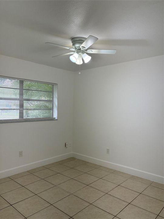 Neutral-toned tile flooring, white wall finish, and a ceiling-mounted fan with integrated light fixture
