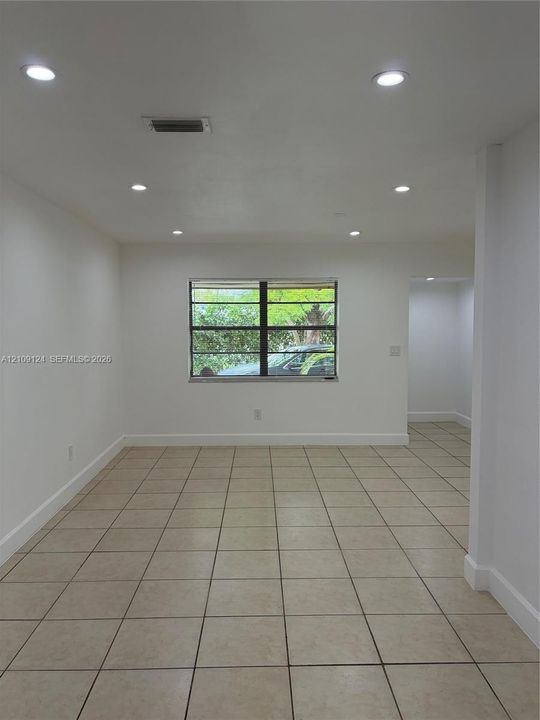 Neutral interior space featuring light-colored tile flooring, recessed ceiling lighting, and a single-pane window