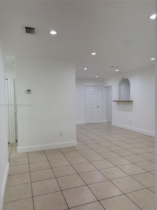 Interior space featuring large-format neutral tile flooring, recessed ceiling lighting, a six-panel door, and a built-in arched wall niche with a wooden ledge