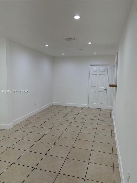Interior space featuring neutral tile flooring, recessed ceiling lighting, a six-panel door, and a built-in wooden shelf