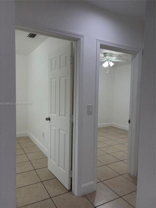 Interior featuring large-format neutral floor tile, six-panel interior doors, and a ceiling-mounted light fixture with a multi-blade fan