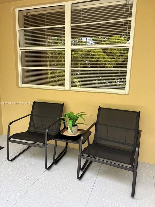 Covered outdoor space featuring large horizontal sliding windows, neutral-toned exterior wall finishes, and light-toned tile flooring
