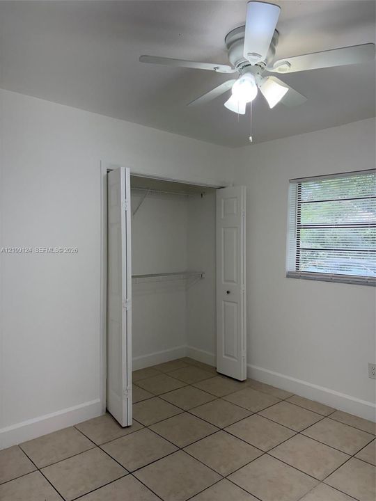 Room featuring ceramic tile flooring, a multi-pane window with horizontal blinds, a ceiling fan with integrated lighting, and a closet with bifold doors