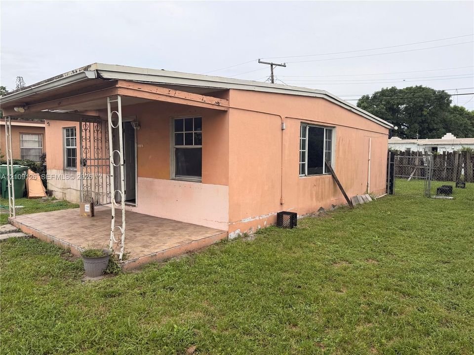 Single-story exterior featuring a covered front porch, decorative metal support columns, stucco siding, and a tiled porch surface