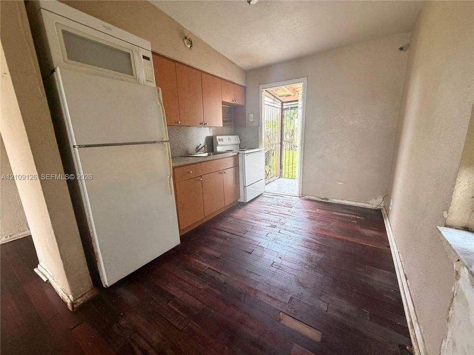 Kitchen featuring wood-finish flooring, built-in cabinetry, white appliance suite, and a door providing exterior access